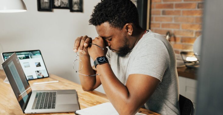 a tired man rubbing his eyes while sitting in front of his laptop